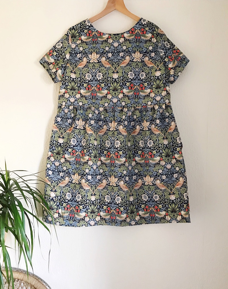 May include: A blue and green short-sleeved dress with a floral print featuring birds and flowers. The dress has a gathered skirt and a round neckline.