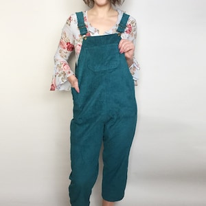 May include: A teal blue corduroy overall with a floral print blouse. The overall has a front pocket and adjustable straps.