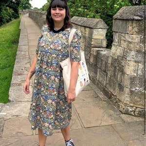 May include: A person wearing a floral print midi dress with a white tote bag and black high-top sneakers. The person is standing on a stone path.