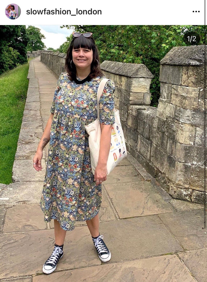 May include: A person wearing a floral print midi dress with a white tote bag and black high-top sneakers. The person is standing on a stone path.