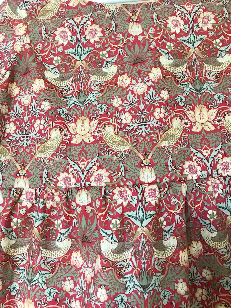 May include: Red fabric with a repeating pattern of stylized birds, flowers, and leaves. The pattern is in shades of green, gold, and white.