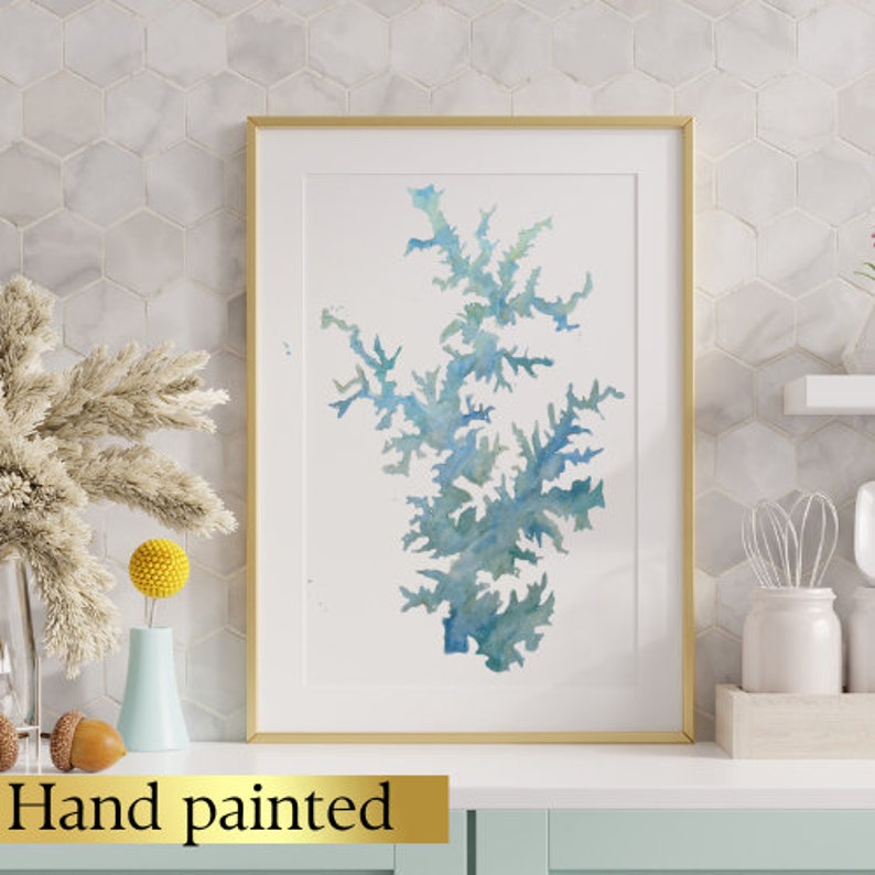 May include: A framed watercolor painting of a blue and green tree-like shape. The painting is on a white background and has a gold frame. The text "Hand painted" is visible below the frame.
