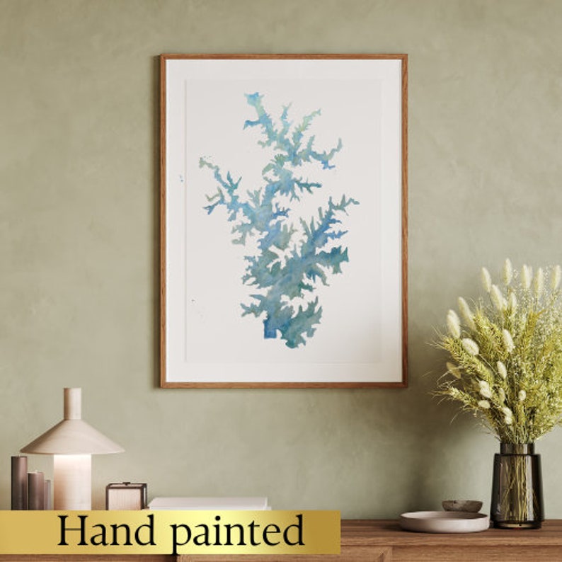 May include: A hand-painted watercolor illustration of a blue and green tree-like shape, framed in a light wood frame. The image is hanging on a light green wall.
