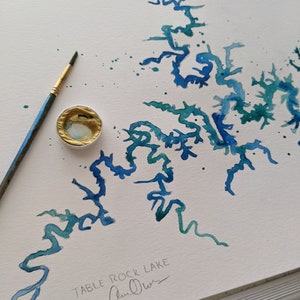 May include: A watercolor painting of Table Rock Lake, a popular destination in the Ozark Mountains. The painting is done in shades of blue and green, with a few splashes of white. The artist's signature, "Ann Oliver", is visible in the bottom right corner.