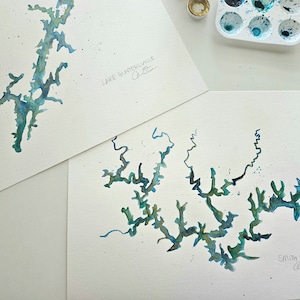 May include: Two watercolor paintings of lakes. The top painting is of Lake Guntersville, Alabama. The bottom painting is of Smith Lake, Alabama.