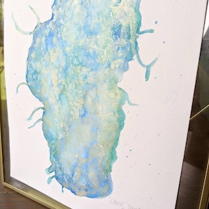 May include: A watercolor painting of Lake Tahoe with gold accents. The painting is framed in a gold frame and signed "Lake Tahoe, Ann Olson".