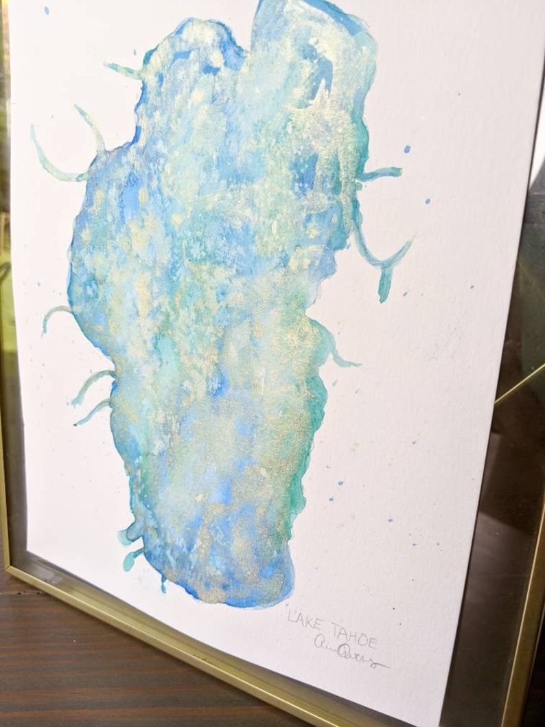 May include: A watercolor painting of Lake Tahoe with gold accents. The painting is framed in a gold frame and signed "Lake Tahoe, Ann Olson".