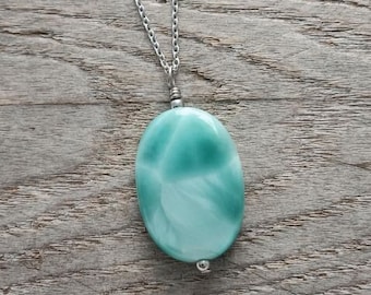May include: A silver chain necklace with a light blue oval pendant. The pendant has a swirling, marbled pattern.