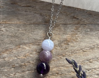 May include: A silver chain necklace with a pendant made of three round beads. The beads are light blue, lavender, and amethyst.