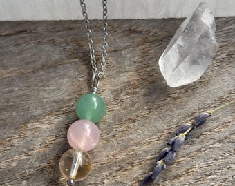 May include: A silver chain necklace with three gemstone beads. The beads are green, pink, and yellow.