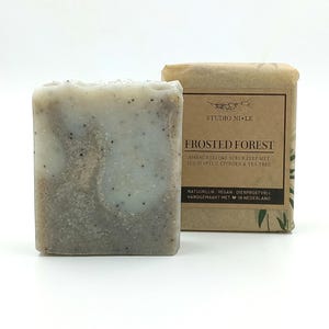 Peut inclure: Un pain de savon rectangulaire à l'aspect givré, à côté d'un emballage. Le savon présente un motif marbré gris clair et brun. L'emballage est marron avec le texte "FROSTED FOREST" et d'autres textes.