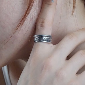 Può includere: Un anello d'argento con più bande, ciascuna con un diverso design testurizzato. L'anello è indossato sull'indice di una mano.
