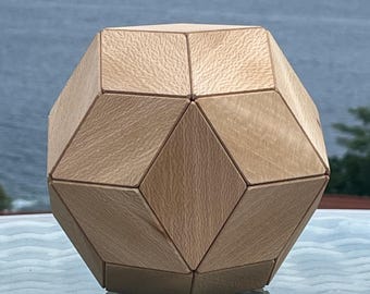 May include: A geometric polyhedral object constructed from light-colored wood with a visible grain. The shape features multiple diamond and triangular facets joined together to form a symmetrical, multi-sided solid structure with smooth edges.