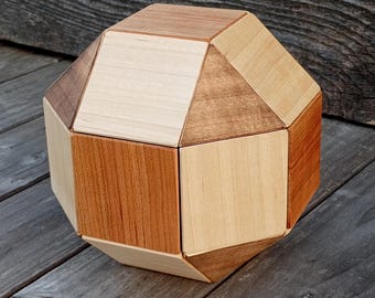 May include: A geometric wooden puzzle with a multi-faceted design. The puzzle is constructed from various shades of wood, including light and dark browns, and beige. The puzzle is resting on a weathered wooden surface.