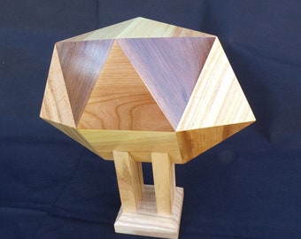 May include: A geometric wooden sculpture with a multi-faceted top in shades of light and dark brown, supported by two vertical posts on a square base. The sculpture is made of various wood types.