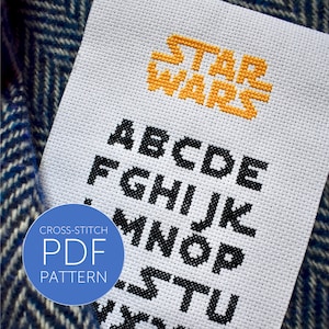 May include: Cross-stitch PDF pattern for a Star Wars alphabet. The letters are black on a white background. The words "Star Wars" are in yellow.