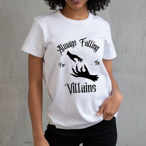 May include: White t-shirt with the text "Always Falling For The Villains" in a gothic font. The graphic features a pair of hands reaching towards each other, one human and one clawed, with a sunburst design.