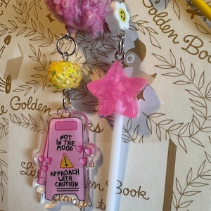 Señal de precaución (rosa). Dije de libro, llavero, clip, dije de diario, marcapáginas, clip.