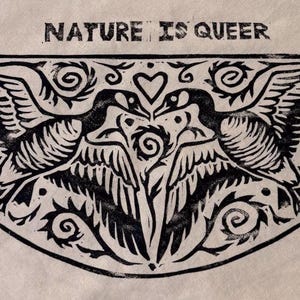 May include: A beige fabric patch featuring a black ink block print of two geese facing each other with wings spread. Above the geese, the text reads NATURE IS QUEER. The design includes decorative swirls, a heart, and a central spiral element.