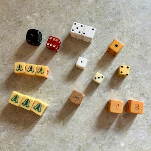 May include: A collection of dice and wooden blocks with various numbers, letters, and symbols. The dice are in different colors, including red, white, black, and cream. The wooden blocks are brown and have the words "LIKE" and "T2" on them.