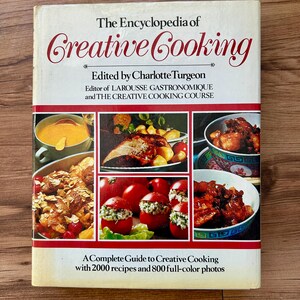 May include: The Encyclopedia of Creative Cooking cookbook with a cream-colored cover. The title is in red script, with images of prepared dishes. The book is edited by Charlotte Turgeon and includes 2,000 recipes and 800 full-color photos.