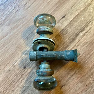 May include: Antique glass door knobs with a brass finish and a metal spindle. The knobs are clear glass with a frosted design.