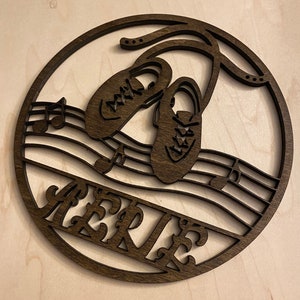 May include: A dark brown wooden round ornament with a cutout design of two dancing shoes, musical notes, and the name "AERIE".