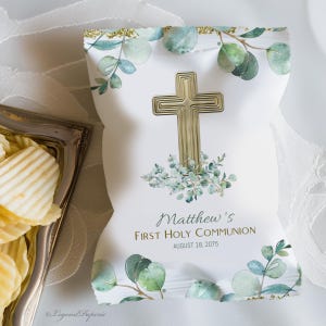 May include: White favor bag with a gold cross and green watercolor leaves. The bag says "Matthew's First Holy Communion August 18, 2075".