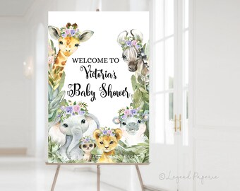May include: Welcome to Victoria's Baby Shower sign with a white background and a jungle theme. The sign features a giraffe, zebra, elephant, lion, and hippo wearing flower crowns. The animals are surrounded by green leaves and flowers.