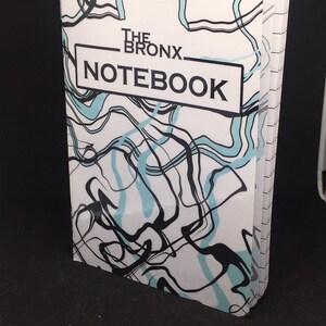 May include: A white notebook with a black and blue abstract design. The cover reads "The Bronx Notebook".