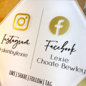 May include: White hexagonal sign with gold Instagram and Facebook logos. The text "Instagram skinbylexie" and "Facebook Lexie Choate-Bewley" is printed below the logos. The text "LIKE|SHARE|FOLLOW|TAG" is printed at the bottom of the sign.
