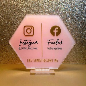 May include: Pink hexagonal sign with gold Instagram and Facebook logos and text. The sign reads "Instagram @leslies_wax_room_ Facebook Leslies Wax Room Like | Share | Follow | Tag".