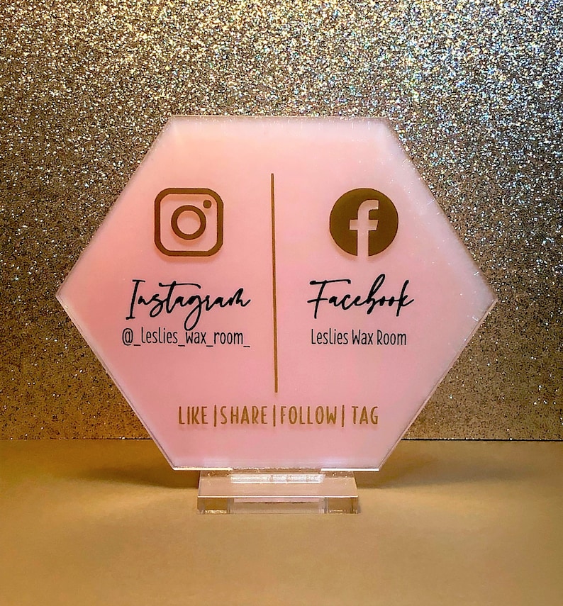 May include: Pink hexagonal sign with gold Instagram and Facebook logos and text. The sign reads "Instagram @leslies_wax_room_ Facebook Leslies Wax Room Like | Share | Follow | Tag".