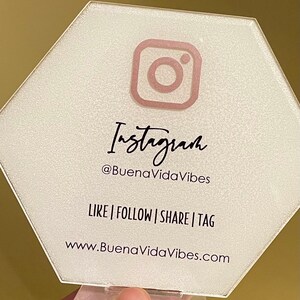 May include: A white hexagonal sign with a pink Instagram logo and the text "Instagram @BuenaVidaVibes LIKE | FOLLOW | SHARE | TAG www.BuenaVidaVibes.com"