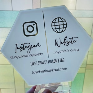May include: White hexagonal sign with black text and icons. The left side says "Instagram" with the Instagram logo and "@Joychristinajewelry". The right side says "Website" with a globe icon and "Joychristina.org". The bottom of the sign says "LIKE | SHARE | FOLLOW | TAG" and "Joychristinaj@aol.com".