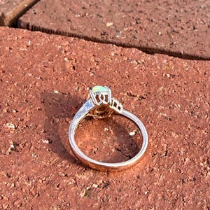 Puede incluir: Un anillo de oro con un &oacute;palo central de forma ovalada en un engaste de garras. La banda es lisa y pulida, con una galer&iacute;a de metal decorativa debajo de la piedra que incluye peque&ntilde;os detalles recortados en los lados del engaste.