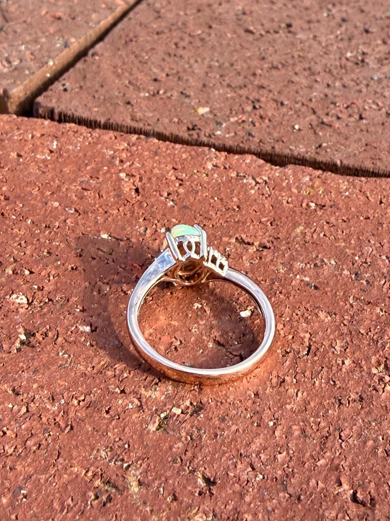 Puede incluir: Un anillo de oro con un &oacute;palo central de forma ovalada en un engaste de garras. La banda es lisa y pulida, con una galer&iacute;a de metal decorativa debajo de la piedra que incluye peque&ntilde;os detalles recortados en los lados del engaste.