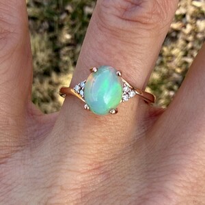 Puede incluir: Un anillo con un &oacute;palo cabuj&oacute;n ovalado montado en una banda de oro rosa pulido. El &oacute;palo central muestra destellos iridiscentes de color verde y naranja. Tres peque&ntilde;as piedras redondas y transparentes est&aacute;n engastadas a cada lado.