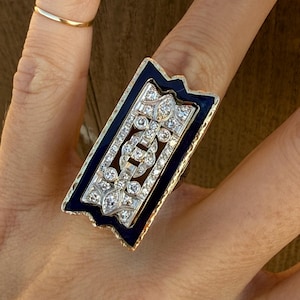 May include: A gold ring with a black enamel rectangular setting featuring a geometric design of diamonds.