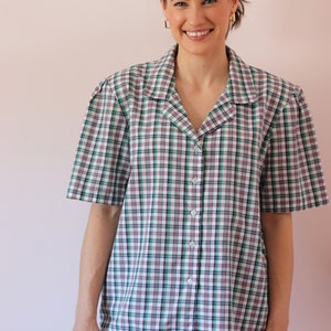 May include: A woman wearing a white, green, and black plaid button-down shirt with short sleeves. She is wearing light blue jeans.