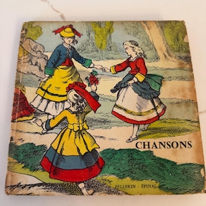May include: Vintage book cover featuring a colorful illustration of three figures in traditional attire dancing in a garden setting. The cover has the word "CHANSONS" and the text "PELLERIN - EPINAL".