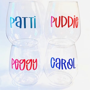 May include: Four clear stemless wine glasses with names in colorful lettering. The names are Patti (blue), Puddie (red), Peggy (red), and Carol (blue). The glasses are arranged in two stacks of two.