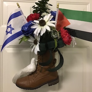 May include: A brown leather boot with a green ribbon and white dove, decorated with flowers and flags of Israel and Palestine.