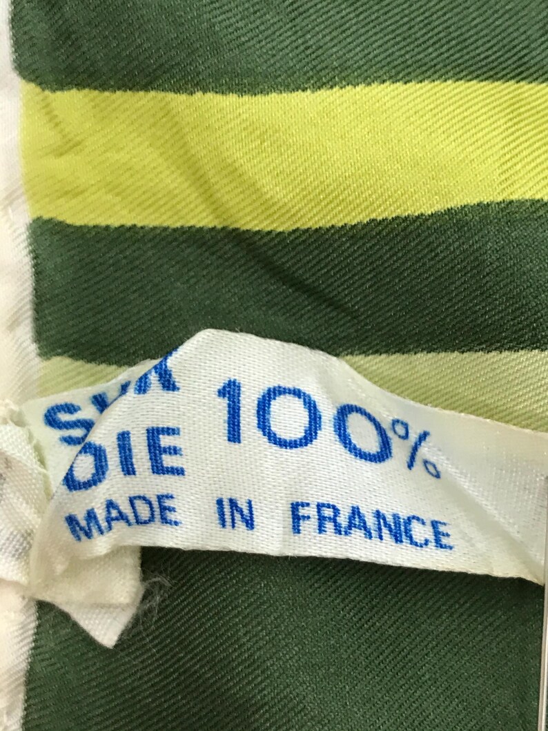 Może przedstawiać: Biała metka z tkaniny z niebieskim tekstem, kt&oacute;ry brzmi "Silk Die 100% Made in France". Metka jest przymocowana do zielono-ż&oacute;łtej tkaniny w paski.