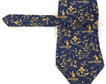 Puede incluir: Una corbata de seda azul marino con un patrón dorado de figuras y edificios estilizados. El patrón se repite en toda la corbata.