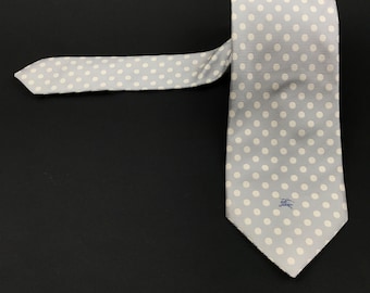 May include: A light gray silk tie with a white polka dot pattern. The tie has a small blue logo with the word "Burberry" on it.