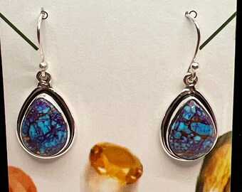 May include: A pair of silver dangle earrings with turquoise blue and purple stones. The earrings are on a white card with the text "JADE BEAR GEMS HANDCRAFTED JEWELRY".