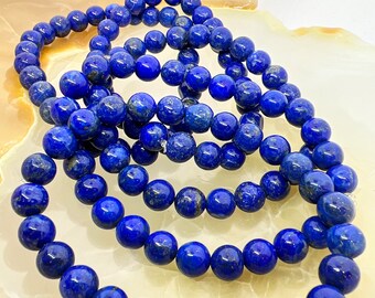 May include: A set of four blue lapis lazuli beaded bracelets. The beads are round and have a smooth, polished finish. The bracelets are stacked on top of each other, creating a layered effect.
