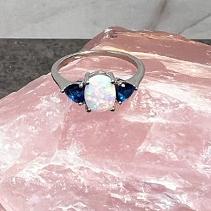 May include: A silver ring with a white opal and two blue sapphire stones.