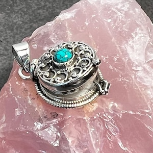 May include: A silver locket pendant with an intricate filigree design and a turquoise gemstone. The locket is open and has a hinged lid.